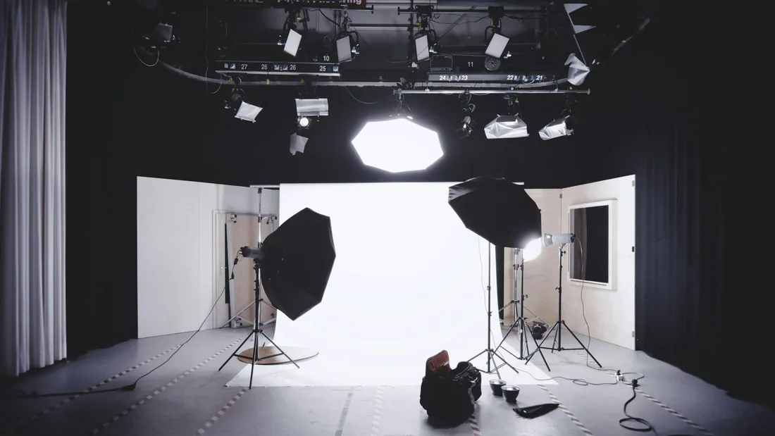 Estudio fotográfico vacío con un fondo blanco iluminado, dos ventanas de luz montadas sobre trípodes y una parrilla de focos en el techo.